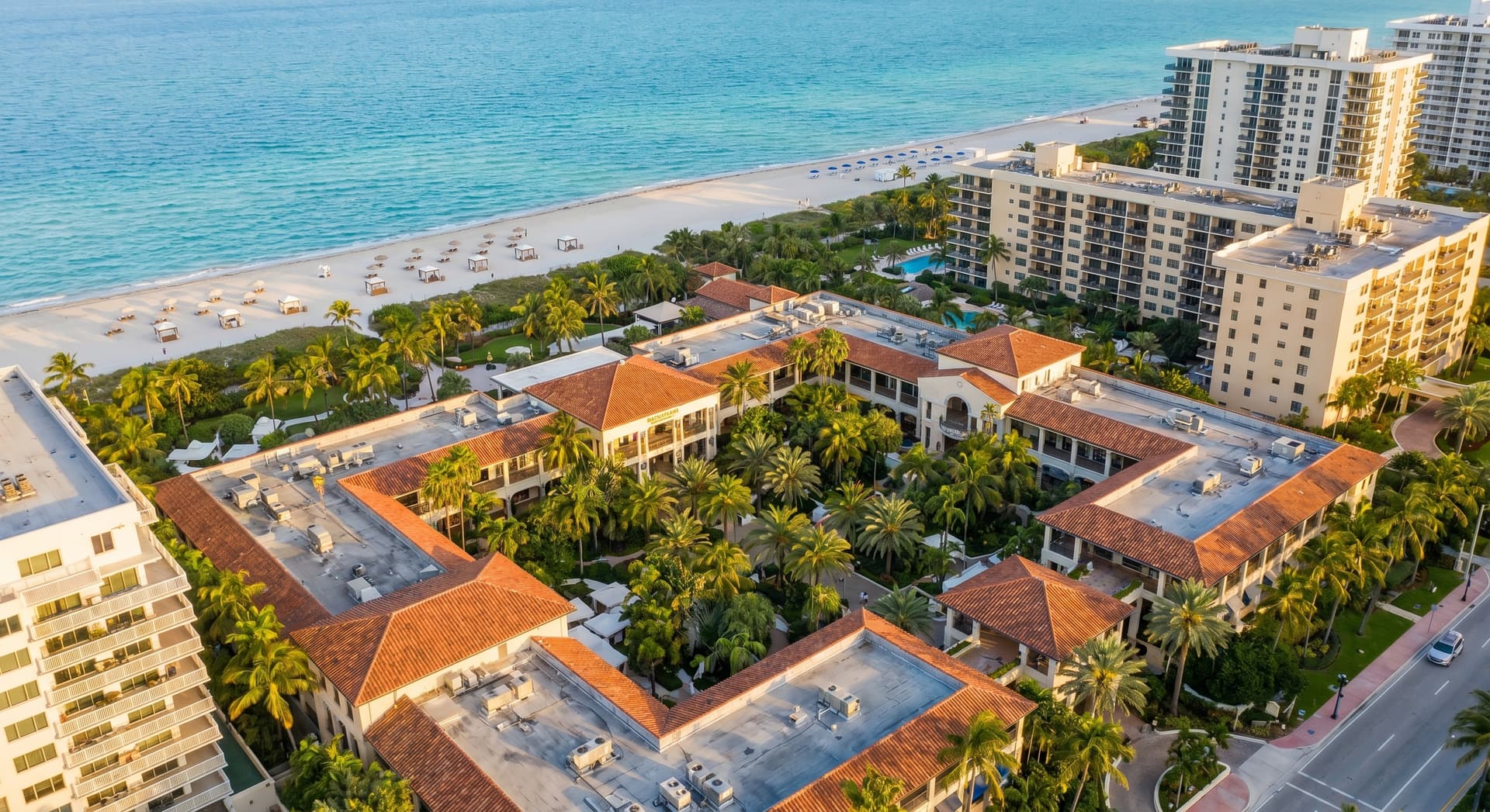 Aerial view of Bal Harbour Beach and the luxury open-air Bal Harbour Shops surrounded by palm trees at golden hour, with turquoise ocean water and white sand