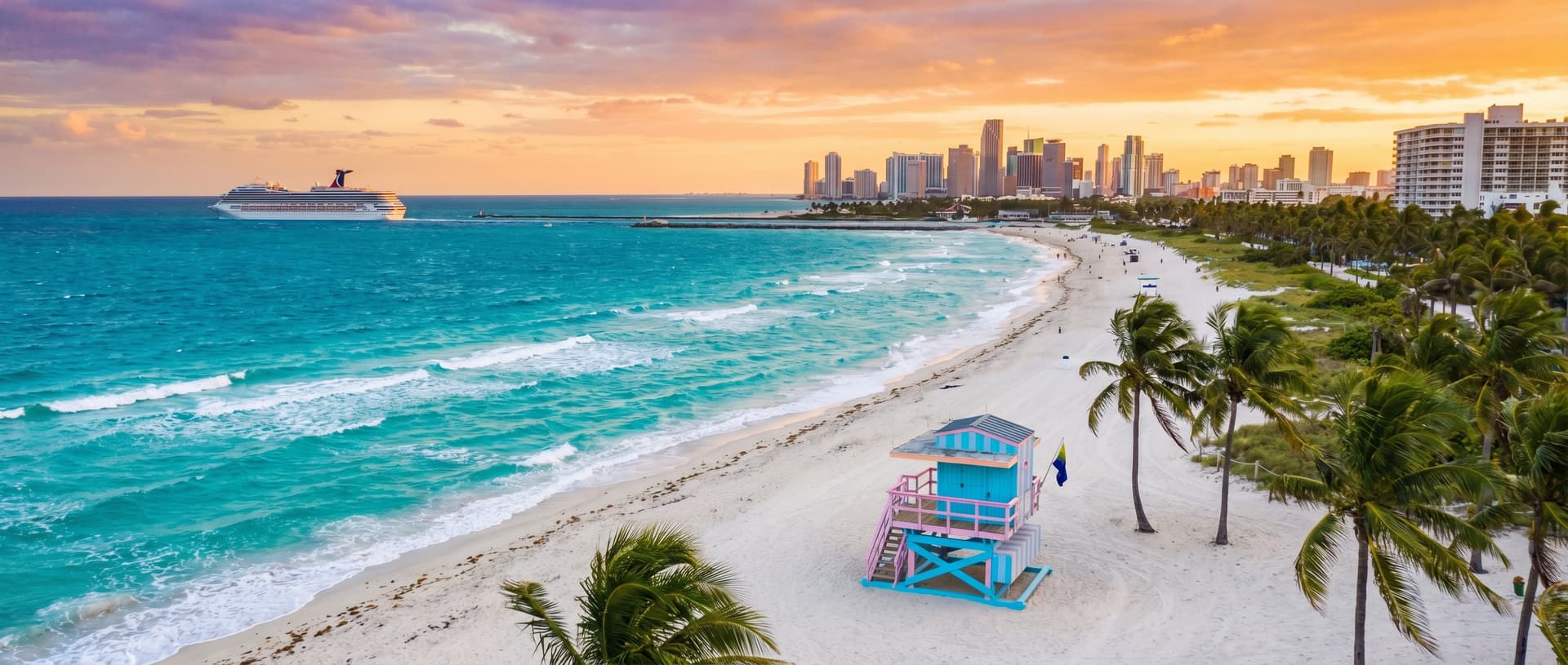 Wide aerial view of iconic Miami beaches at golden hour with turquoise Atlantic water meeting white sand, a pastel art deco lifeguard tower in the foreground, palm trees, and the distant Miami skyline with a cruise ship leaving Government Cut