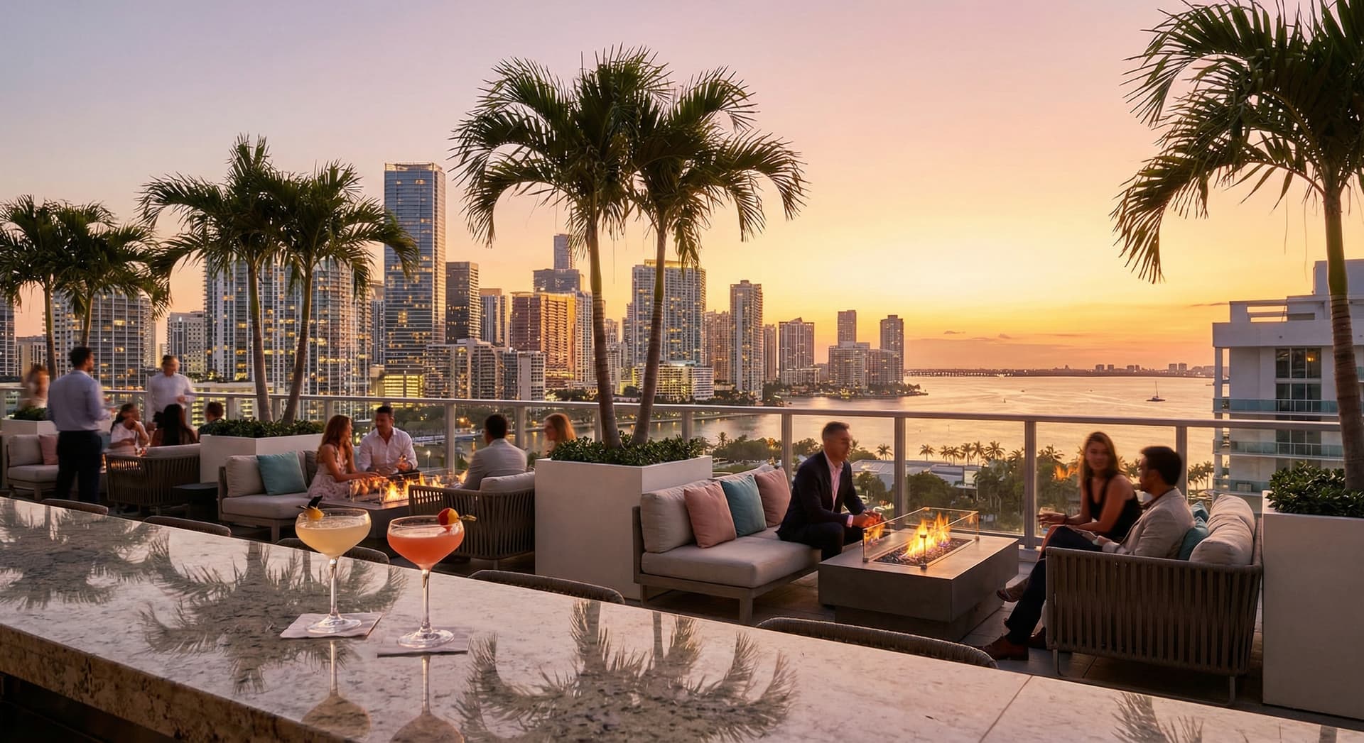 Rooftop bar in Miami's Brickell neighborhood at golden hour with cocktail glasses on a sleek counter, panoramic skyline of glowing high-rise towers, Biscayne Bay in the background, warm orange and pink sunset sky, palm trees, and stylish outdoor lounge seating
