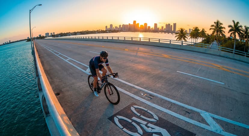 Cyclist riding along the Rickenbacker Causeway bridge in Miami at golden hour with turquoise Biscayne Bay below and the city skyline in the background