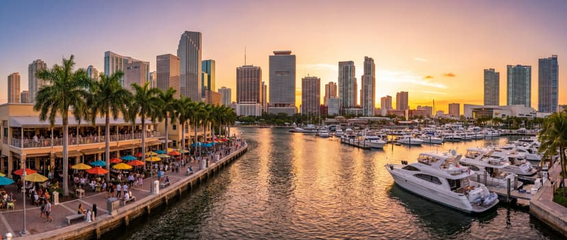Panoramic view of the Miami River at golden hour with waterfront restaurants, docked yachts, and downtown skyscrapers reflecting warm sunset light