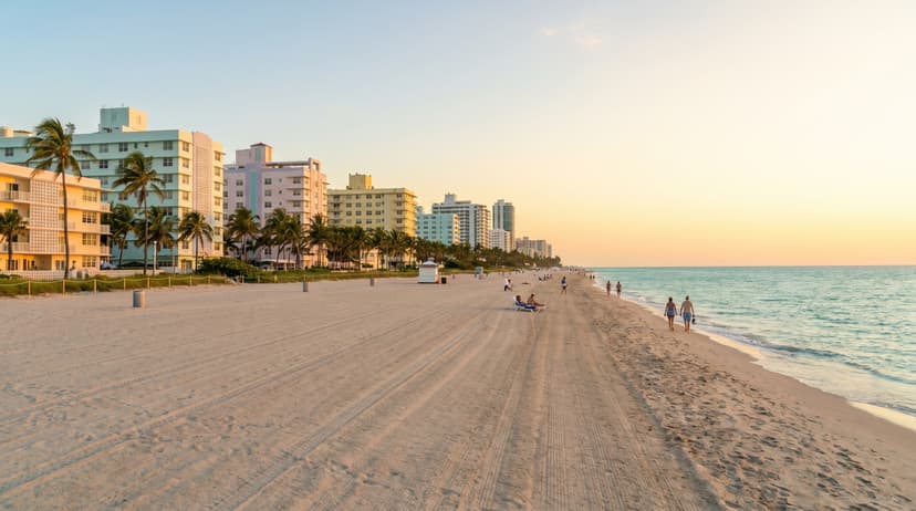 Wide view of North Beach Miami oceanfront at golden hour with sandy beach, palm trees, and vintage MiMo mid-century modern buildings along Collins Avenue
